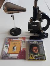 Zdjęcie przedstawia mikroskop oraz okładki książek o Marii Skłodowskiej-Curier